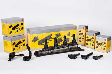 Six NGK ignition coil yellow boxes, in front of them different ignition coil types are placed