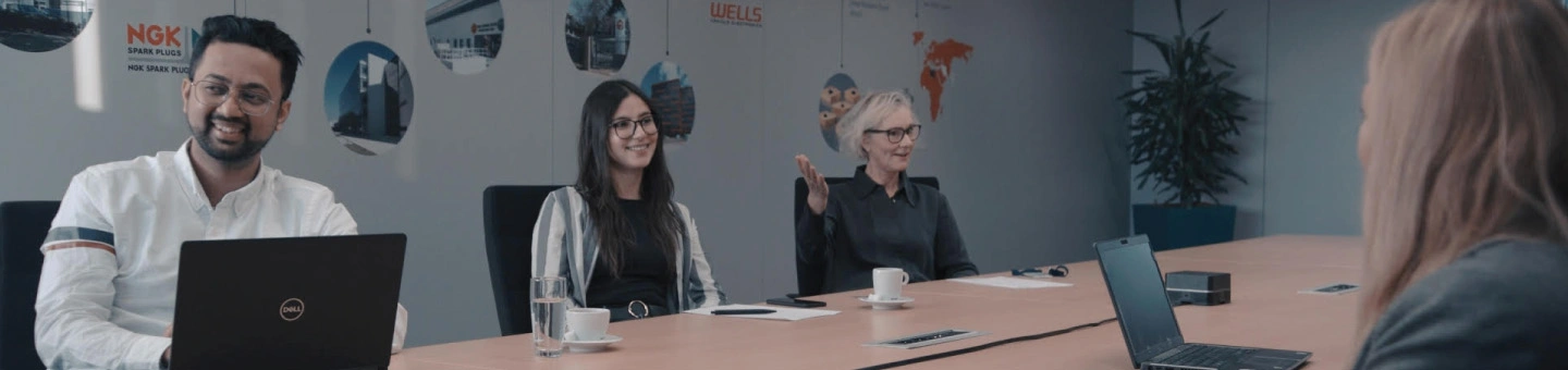 Four chatting people sitting in a meeting room with laptops and coffee
