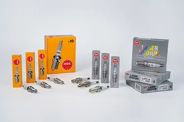Spark plugs in front of their packaging on a white background