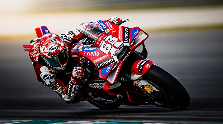 MotoGP motorcyclists on a race track, riding into a corner on a red bike