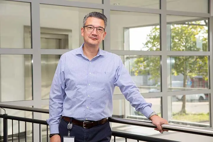 Oliver Kim standing on a gallery wearing a lilac shirt