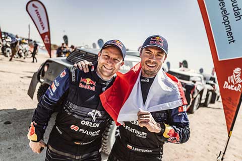 Driver and co-pilot standing in front of the Rally car happily after finishing