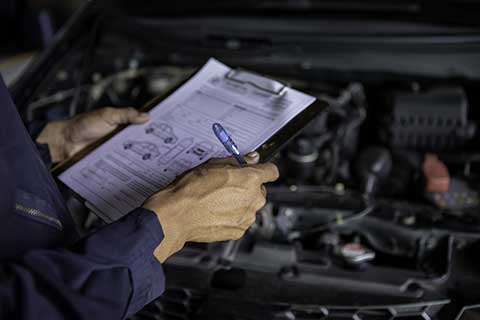 Person checking a list in a garage, car in the background