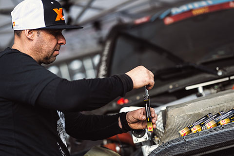 A mechanic i a black shirt opening a NGK glow plug box and pulling out a NGK glow plug